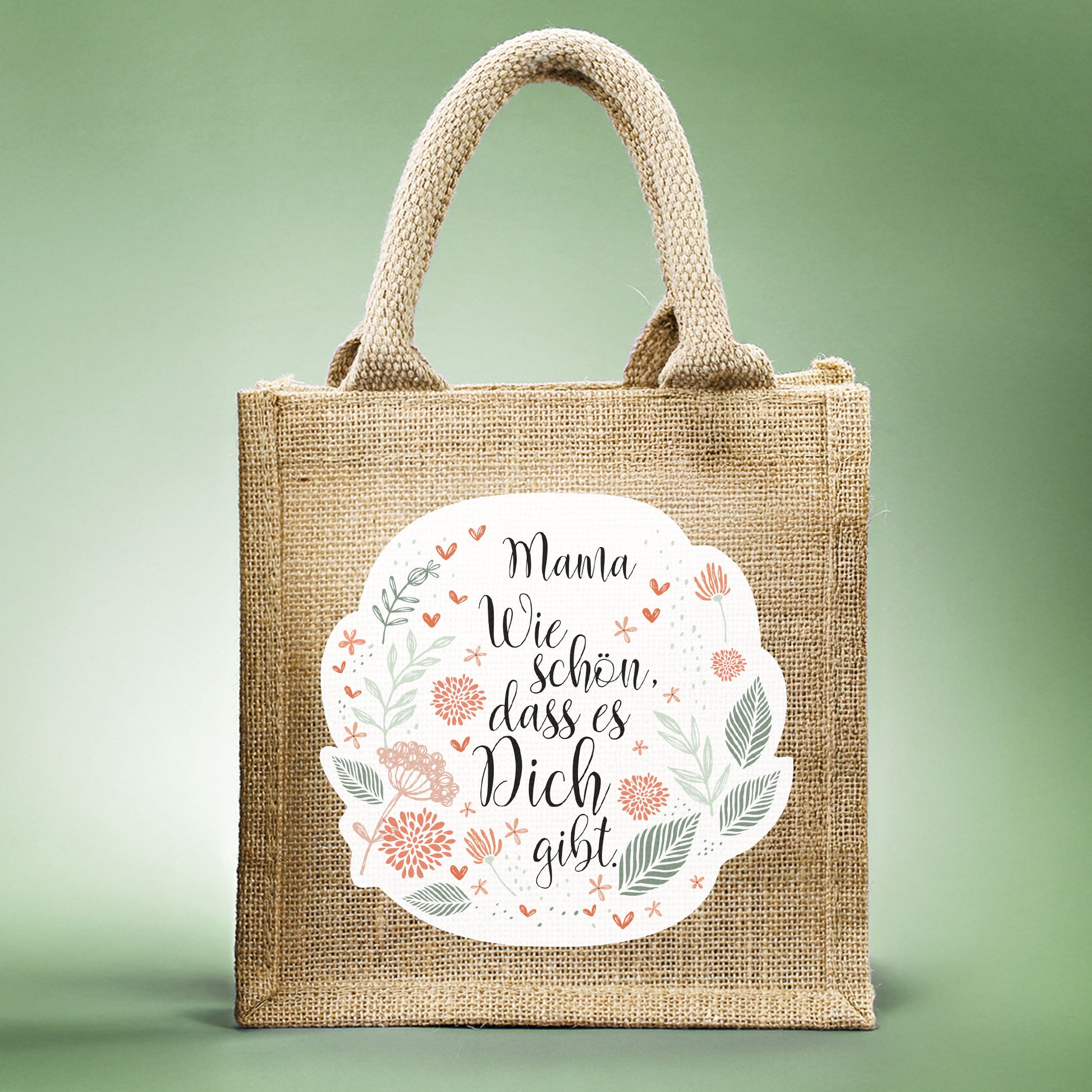 Geschenktasche aus Jute mit floralem Design, dem Spruch „Wie schön, dass es dich gibt.“ und personalisiertem Namen, frontal fotografiert.