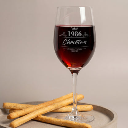 Leonardo Weinglas mit Gravur „1986 Christian – Zur Perfektion gereift“, mit Rotwein gefüllt auf einem Tablett mit Gebäck