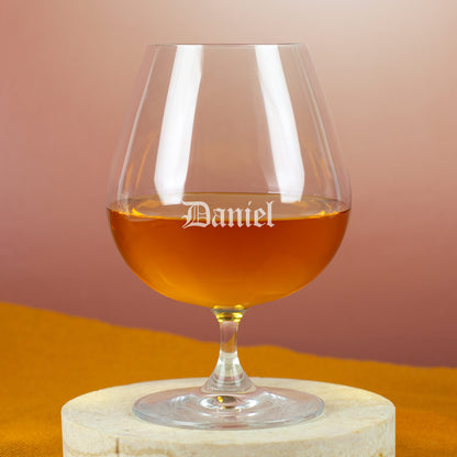 Personalisierter Cognacschwenker mit Gravur „Daniel“ in Frakturschrift – auf hellem Holzuntergrund mit gelbem Tuch.