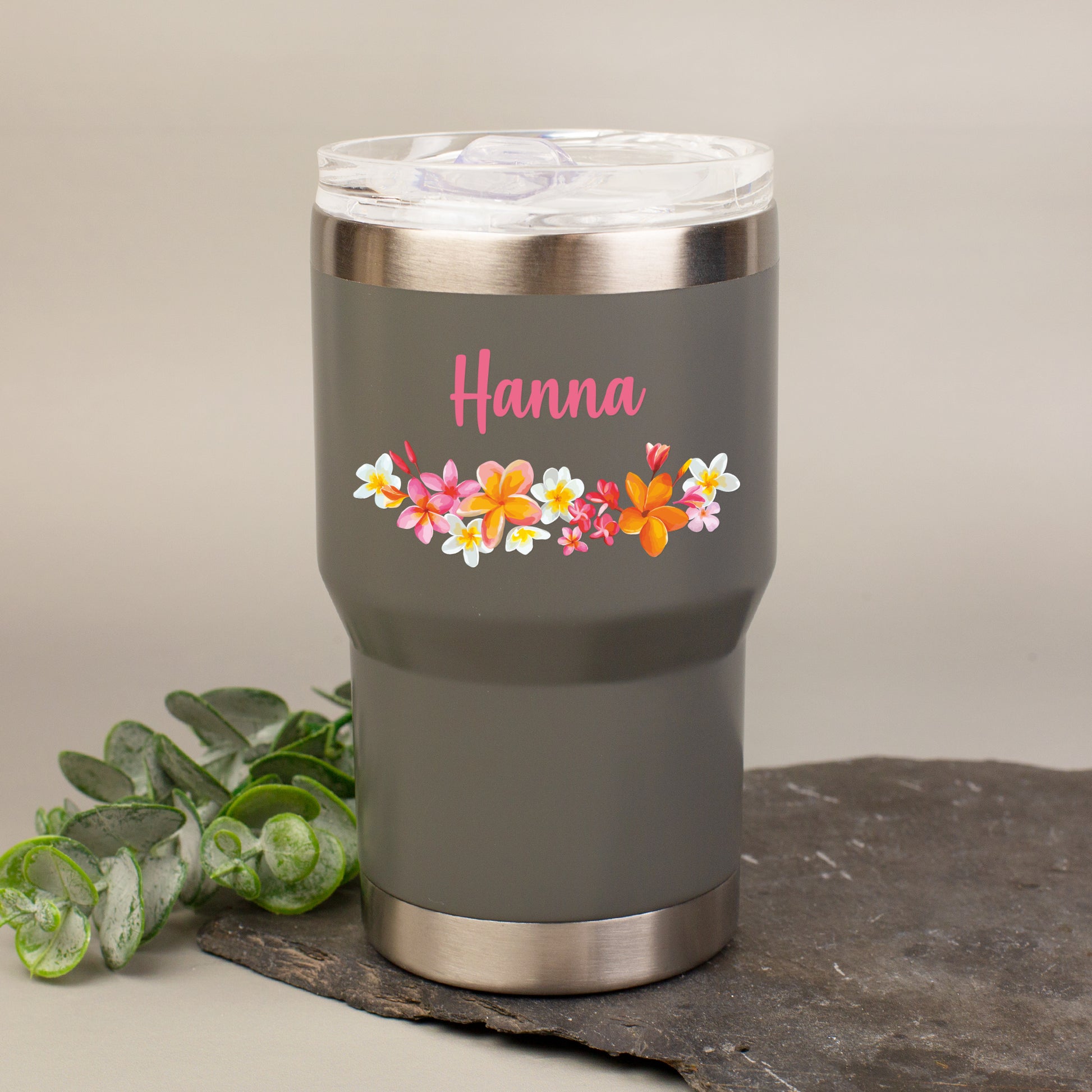 Personalisierter Thermobecher in Grau mit Blumenmotiv und Name Hanna auf dekorativer Steinplatte