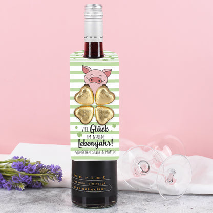 Flaschenanhänger mit grün-weißem Streifendesign, Kleeblättern, Glücksschwein und vier goldenen Lindt Schokoladenherzen, an einer Flasche befestigt.