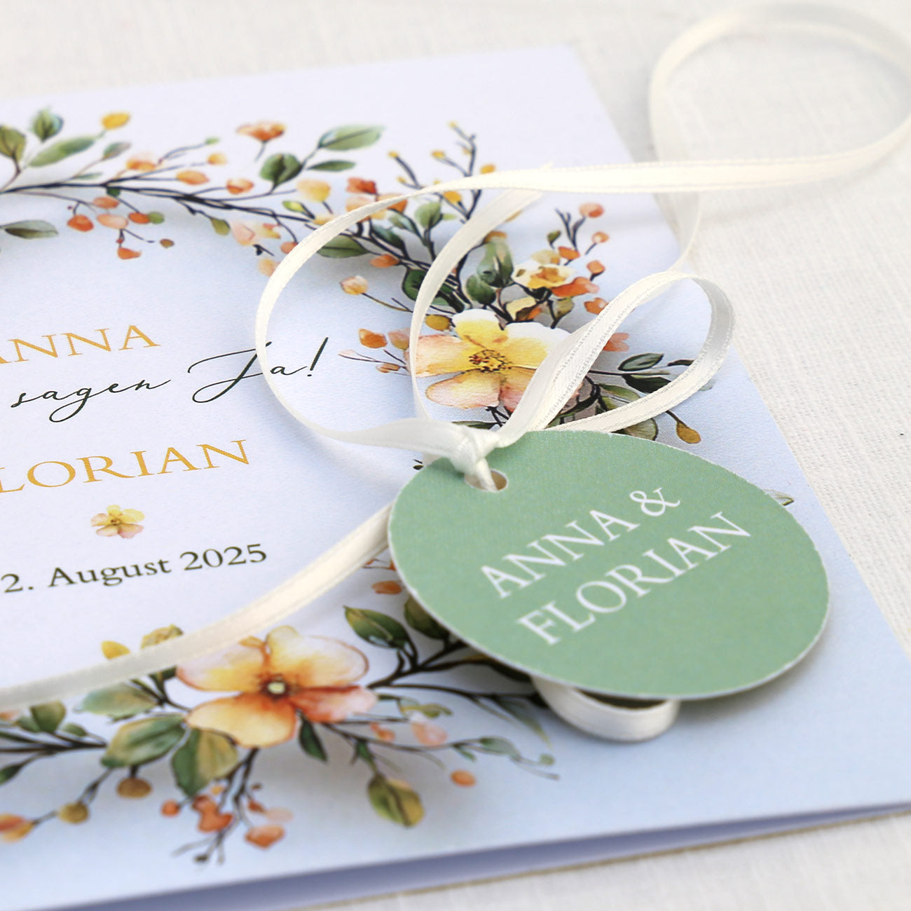Einladungskarte zur Hochzeit mit Blütenkranz und rundem Anhänger