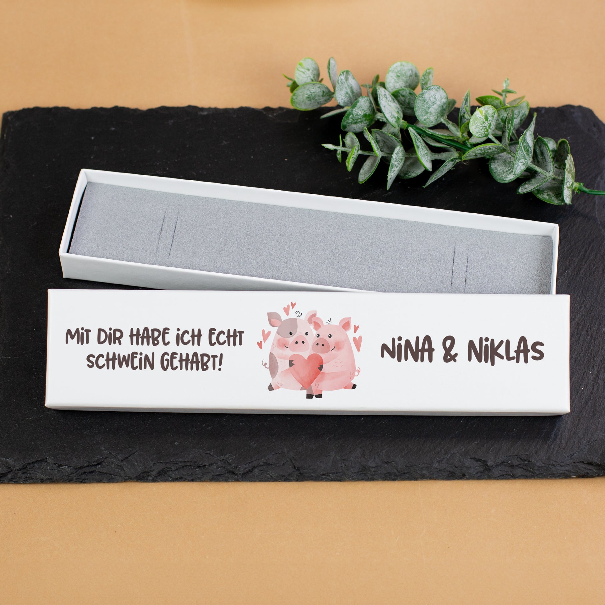 Schmuckverpackung mit Schweinchen-Motiv und Namen auf schwarzer Schieferplatte als Geschenkbox für Schmuck