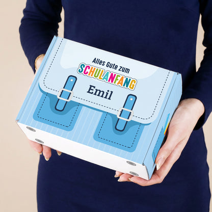 Kleine blaue Geschenkverpackung zum Schulanfang mit Name bedruckt, von einer Person gehalten