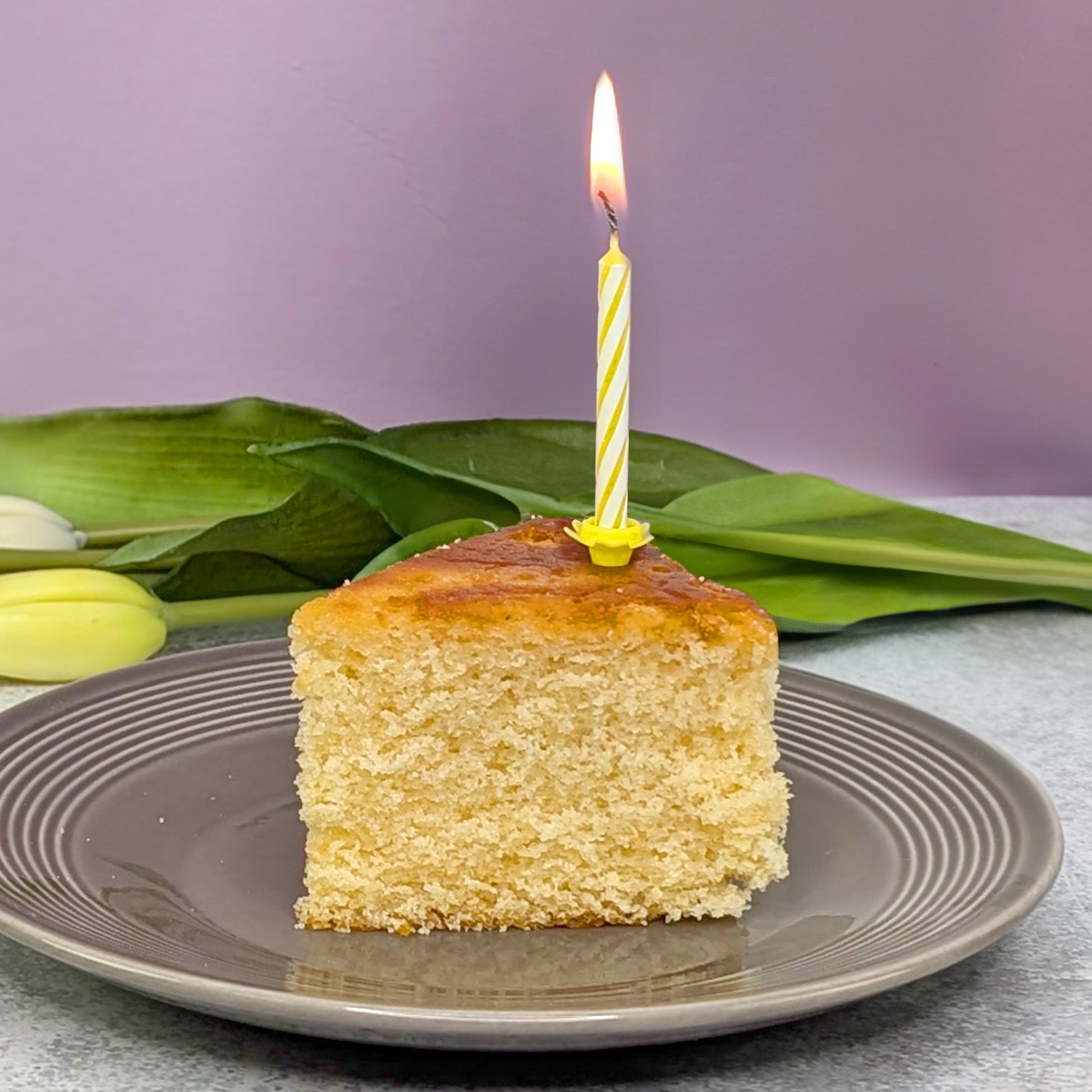 Zitronenkuchen Stück mit Kerze und Tulpen im Hintergrund