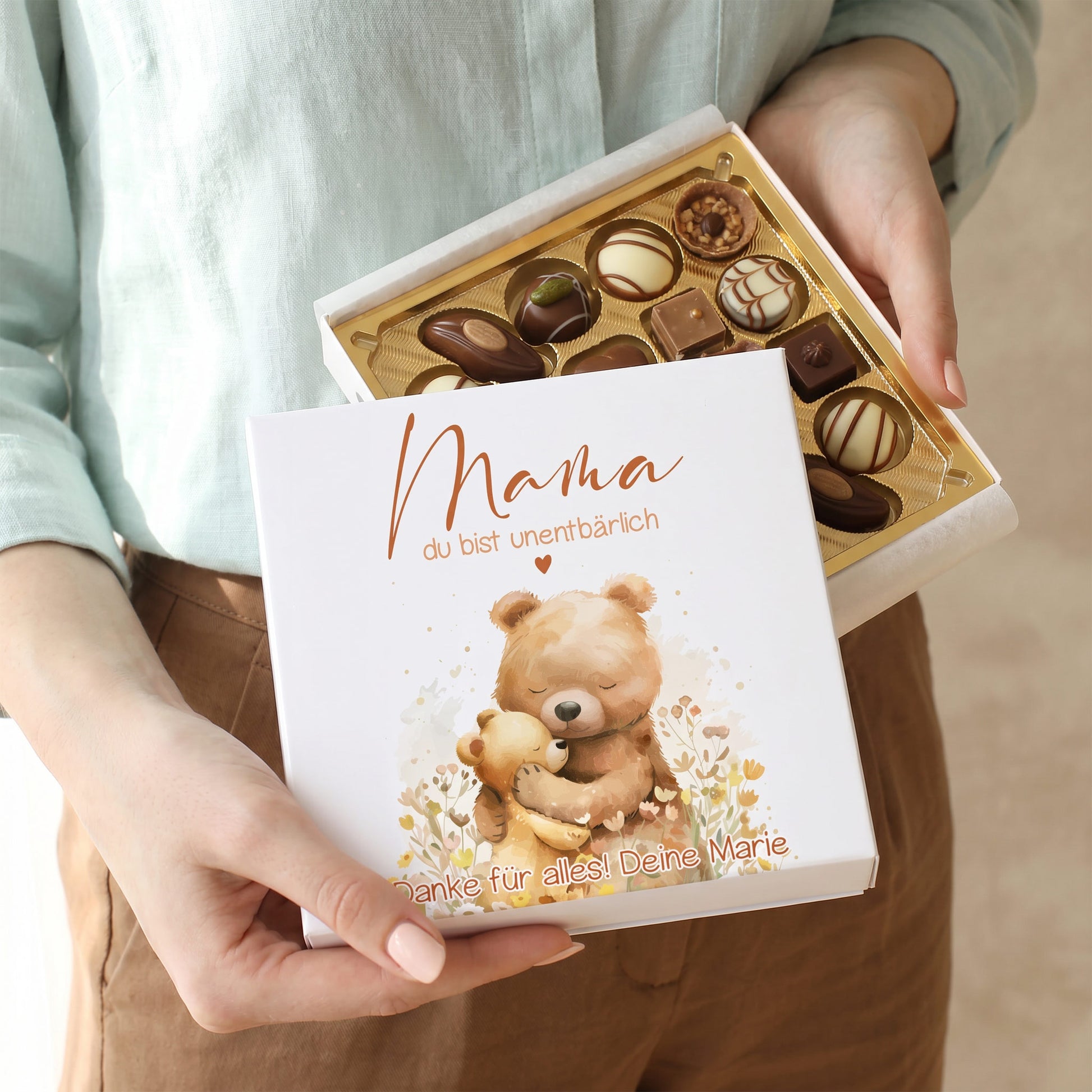 Geöffnete Pralinenbox mit Lindt Mini-Pralinés und personalisiertem Deckel mit Bärenmotiv in der Hand gehalten