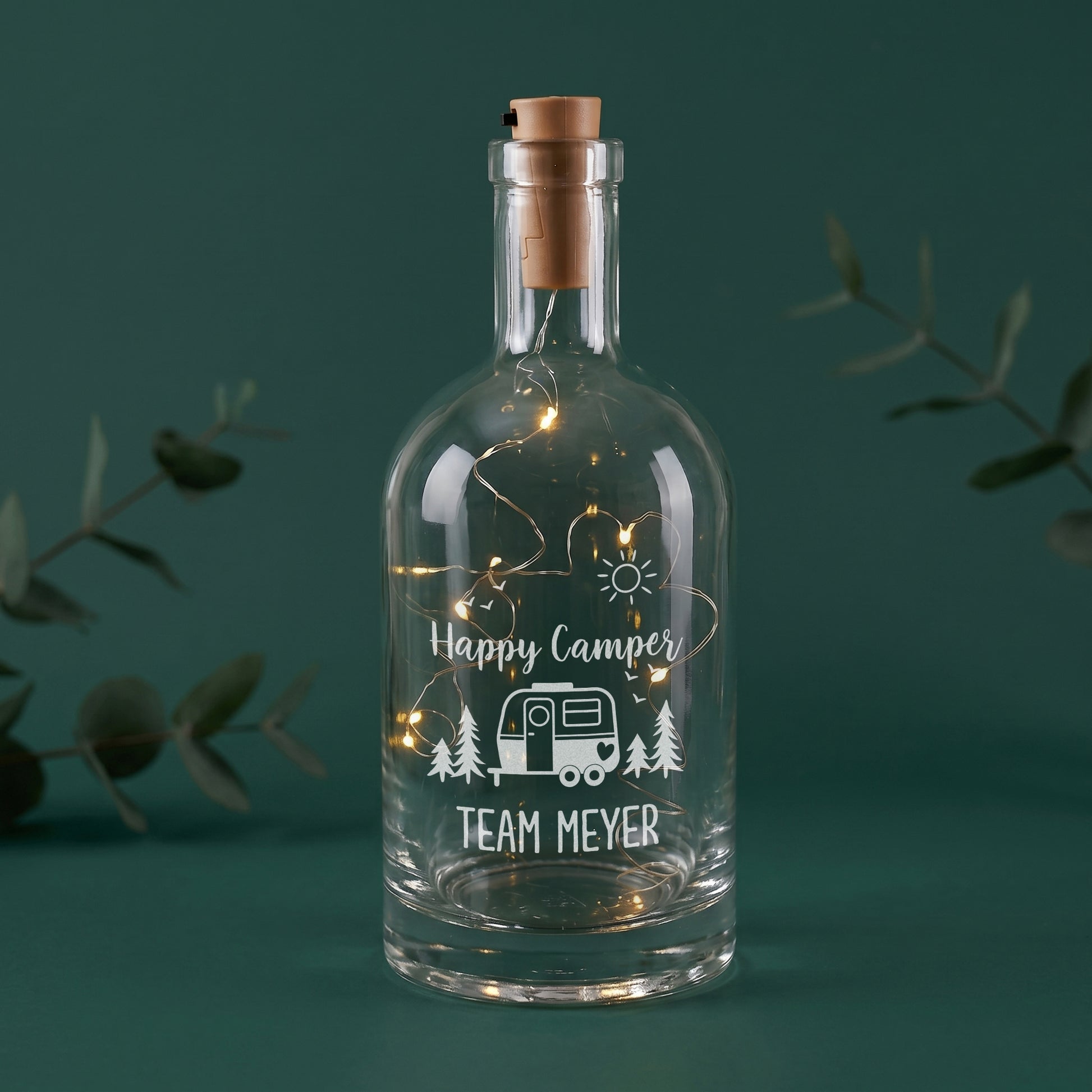 LED-Flaschenlicht aus Glas mit Happy Camper Motiv, Wohnwagen und Wunschtext Team Meyer auf grünem Hintergrund