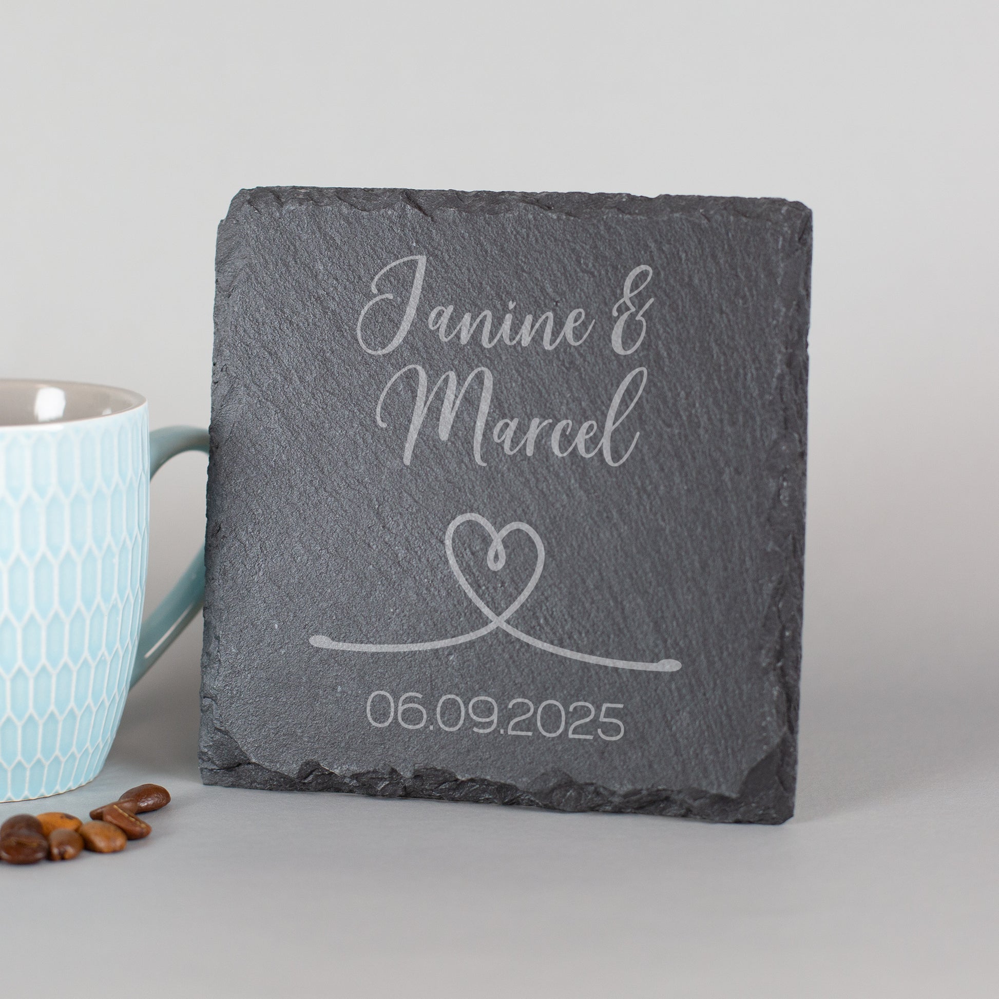 Personalisierter Schiefer-Untersetzer mit Namen und Hochzeitsdatum – angelehnt neben Tasse und Kaffeebohnen
