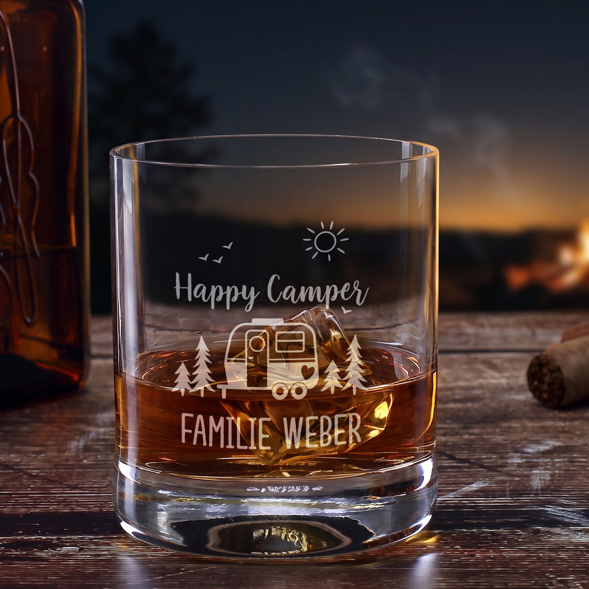 Personalisiertes Whiskeyglas mit Campingmotiv Happy Camper und Wunschtext Familie Weber vor Lagerfeuerkulisse