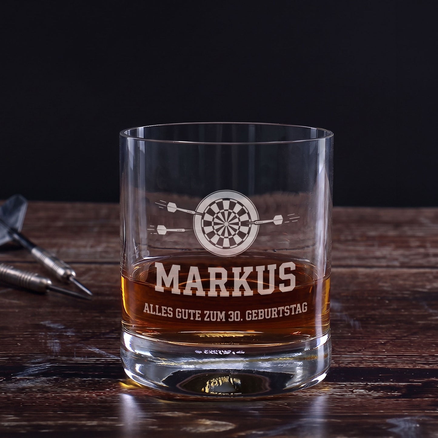 Whiskeyglas mit Dart-Gravur, Name Markus und Wunschtext Alles Gute zum 30. Geburtstag auf Holztisch