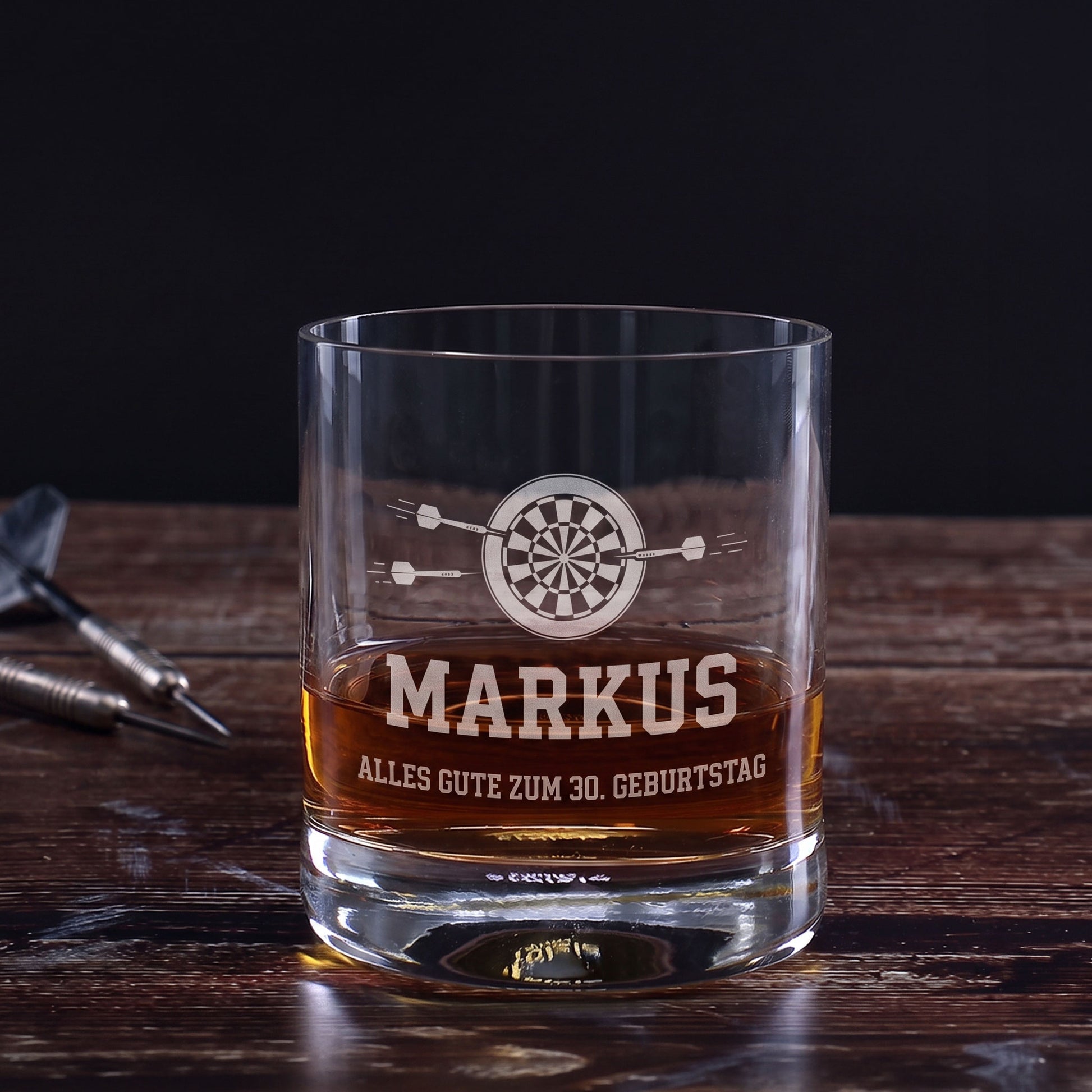 Whiskeyglas mit Dart-Gravur, Name Markus und Wunschtext Alles Gute zum 30. Geburtstag auf Holztisch