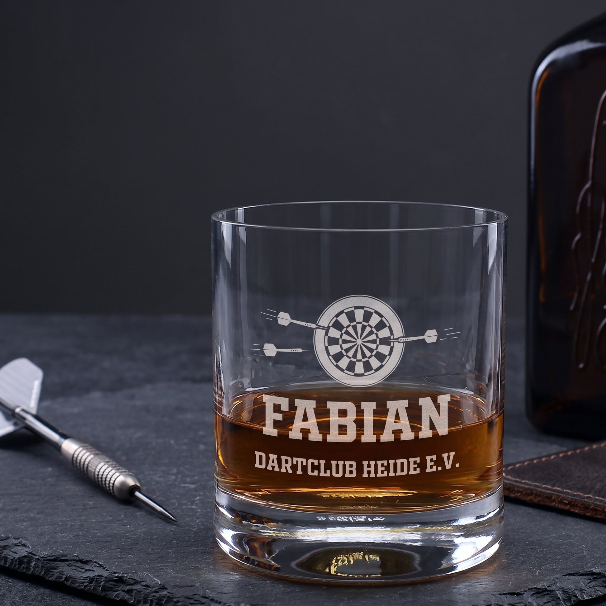 Personalisiertes Whiskyglas mit Dartscheibe, Name Fabian und Wunschtext Dartclub Heide e.V. neben Dartpfeil