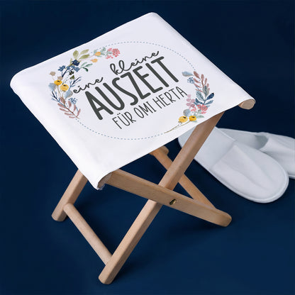 Klapphocker mit Blumenmotiv „eine kleine Auszeit für Omi Herta“ auf blauem Hintergrund