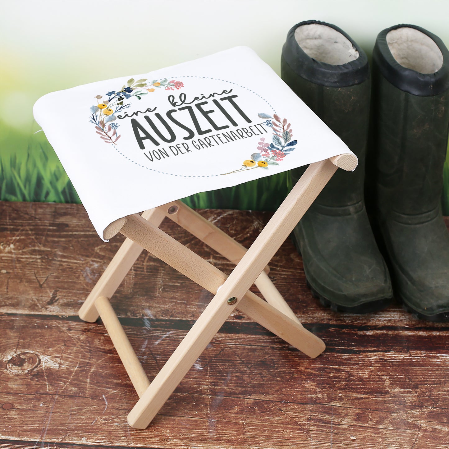 Klapphocker mit Motiv „eine kleine Auszeit von der Gartenarbeit“ neben Gummistiefeln