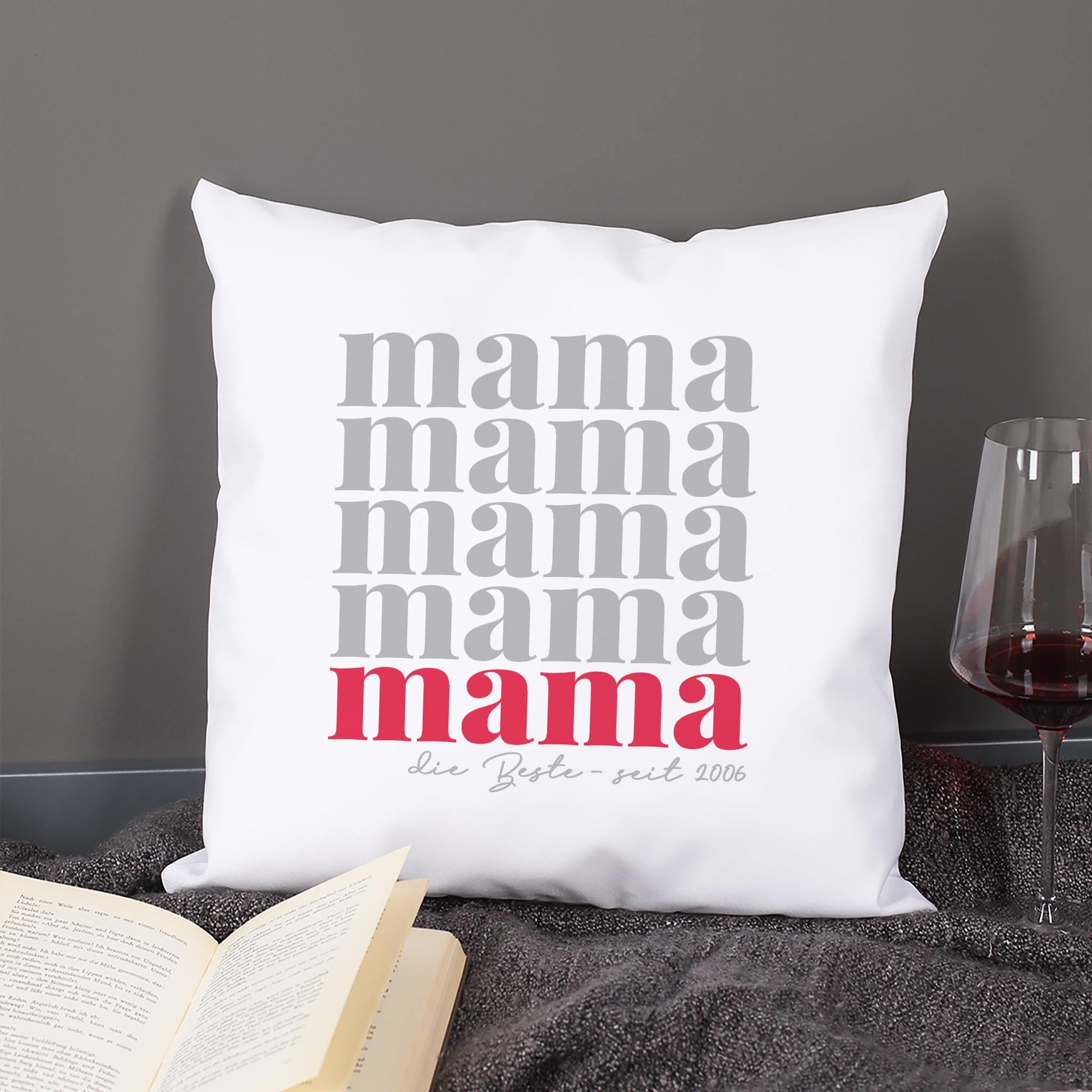 Dekokissen Mama mit Wunschtext im Wohnzimmer neben Buch und Weinglas