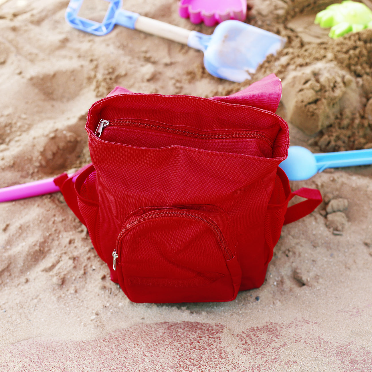 Geöffneter roter Kinderrucksack mit Hauptfach, Außentasche und seitlichem Netzfach auf dem Spielplatz