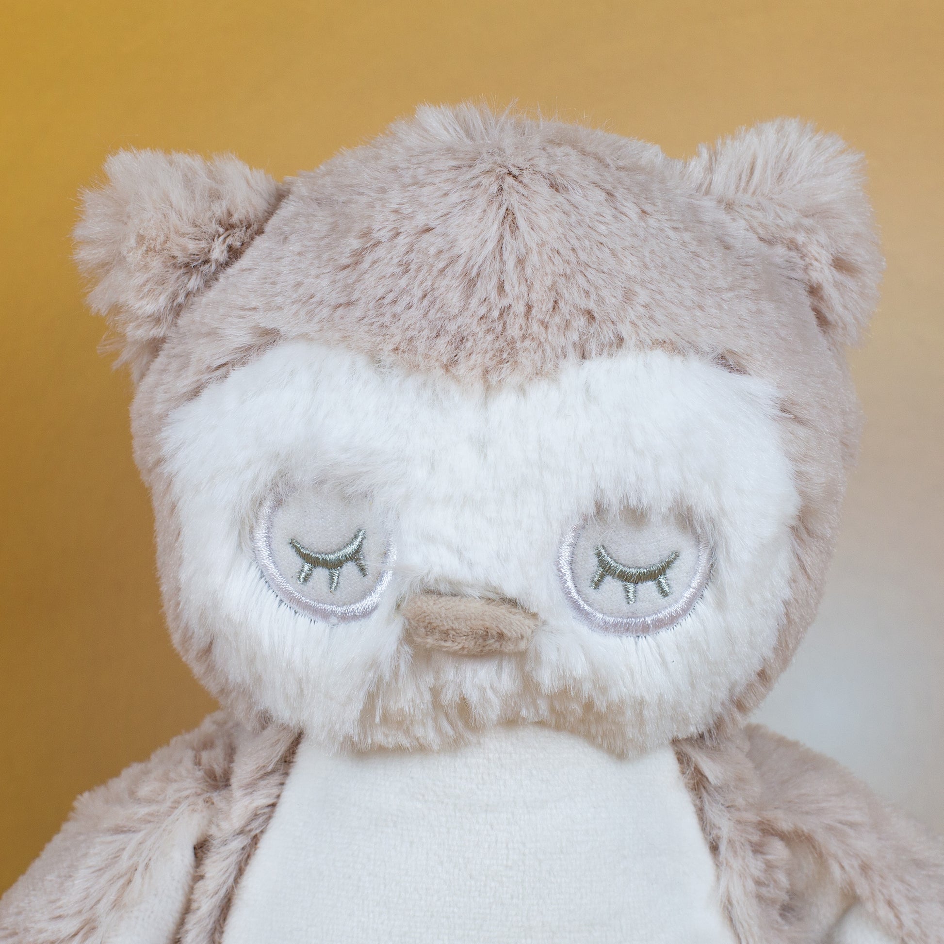 Nahaufnahme des Gesichts der Eule mit geschlossenen Augen, gestickten Wimpern und einem kleinen, beigen Schnabel. Das flauschige Fell ist in hellen Creme- und Beigetönen gehalten.