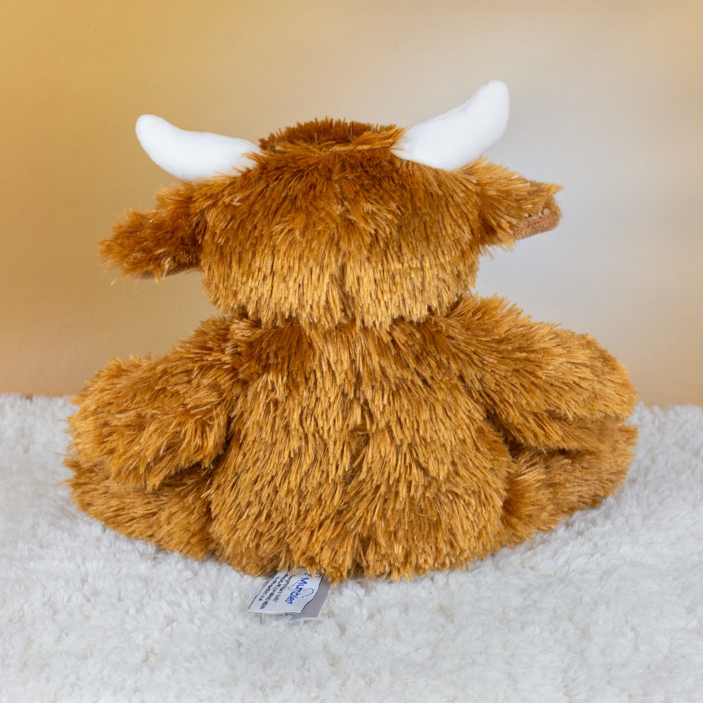 Rückansicht der flauschigen Kuscheltier-Kuh mit braunem Plüschfell, kleinen Hörnern und hellem Hintergrund, Fokus auf die Struktur des Fells.