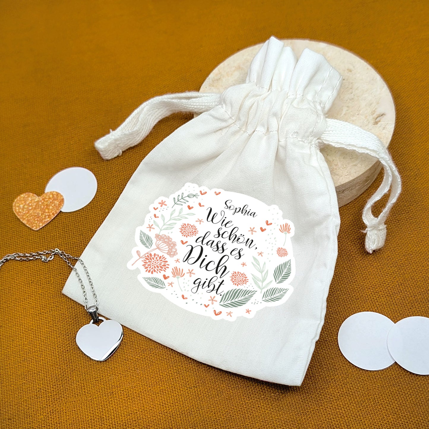 Bedruckter Geschenkbeutel mit Blumenmotiv und Name – Spruch „Wie schön, dass es dich gibt“ – auf Geschenkunterlage mit Herzanhänger