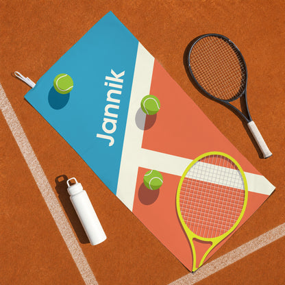 Personalisiertes Tennis Sporthandtuch mit Name Jannik auf Tennisplatz neben Tennisschläger und Trinkflasche