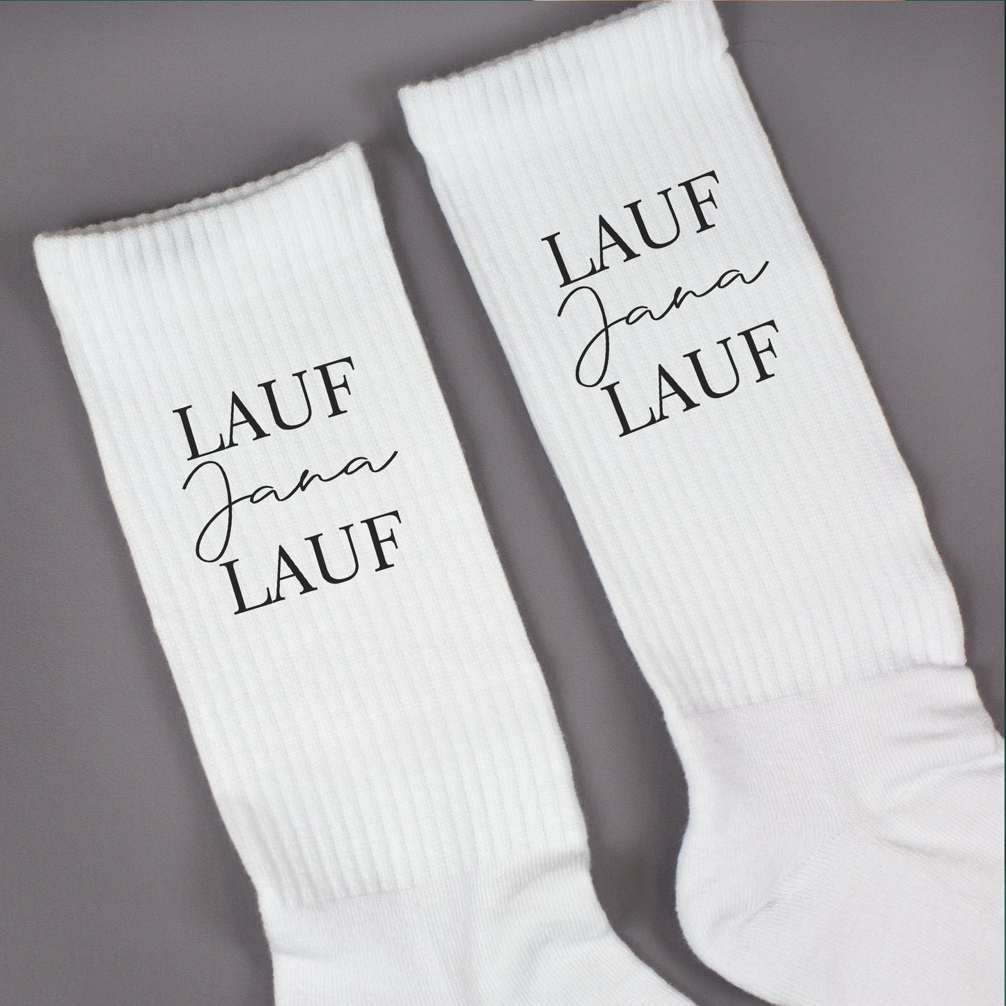 Nahaufnahme von weißen Socken mit „Lauf Jana Lauf“-Aufdruck und gerippter Struktur