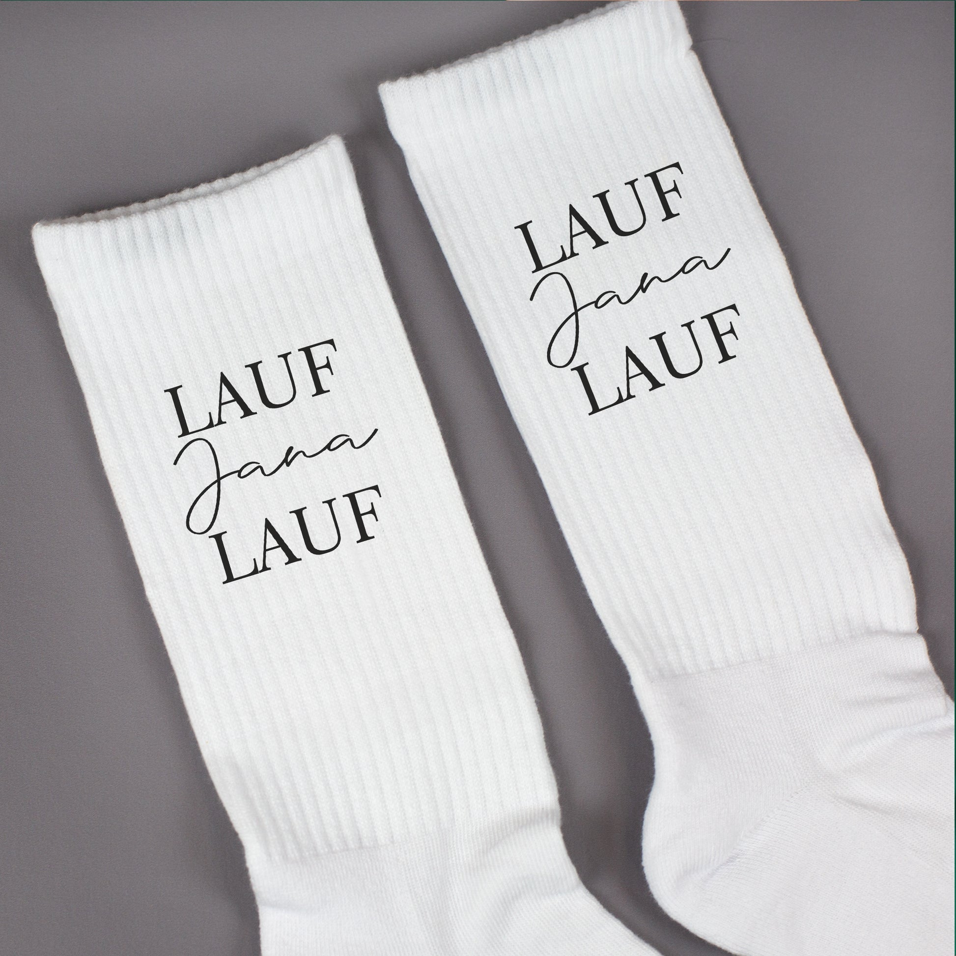 Nahaufnahme von weißen Socken mit „Lauf Jana Lauf“-Aufdruck und gerippter Struktur