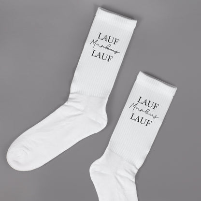 Paar weiße Sportsocken mit personalisiertem „Lauf Markus Lauf“-Aufdruck auf grauem Hintergrund