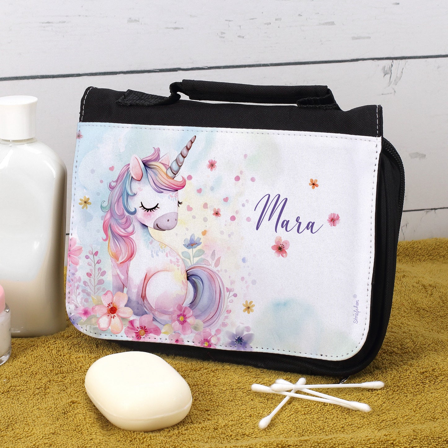 Kinder-Kulturbeutel mit Einhornmotiv und Name „Mara“ – Szene im Badezimmer auf gelbem Handtuch