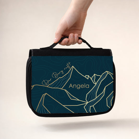 Personalisierter schwarzer Kulturbeutel mit Berge-Aufdruck, Schriftzug Der Berg ruft und Name Angela, getragen am Griff