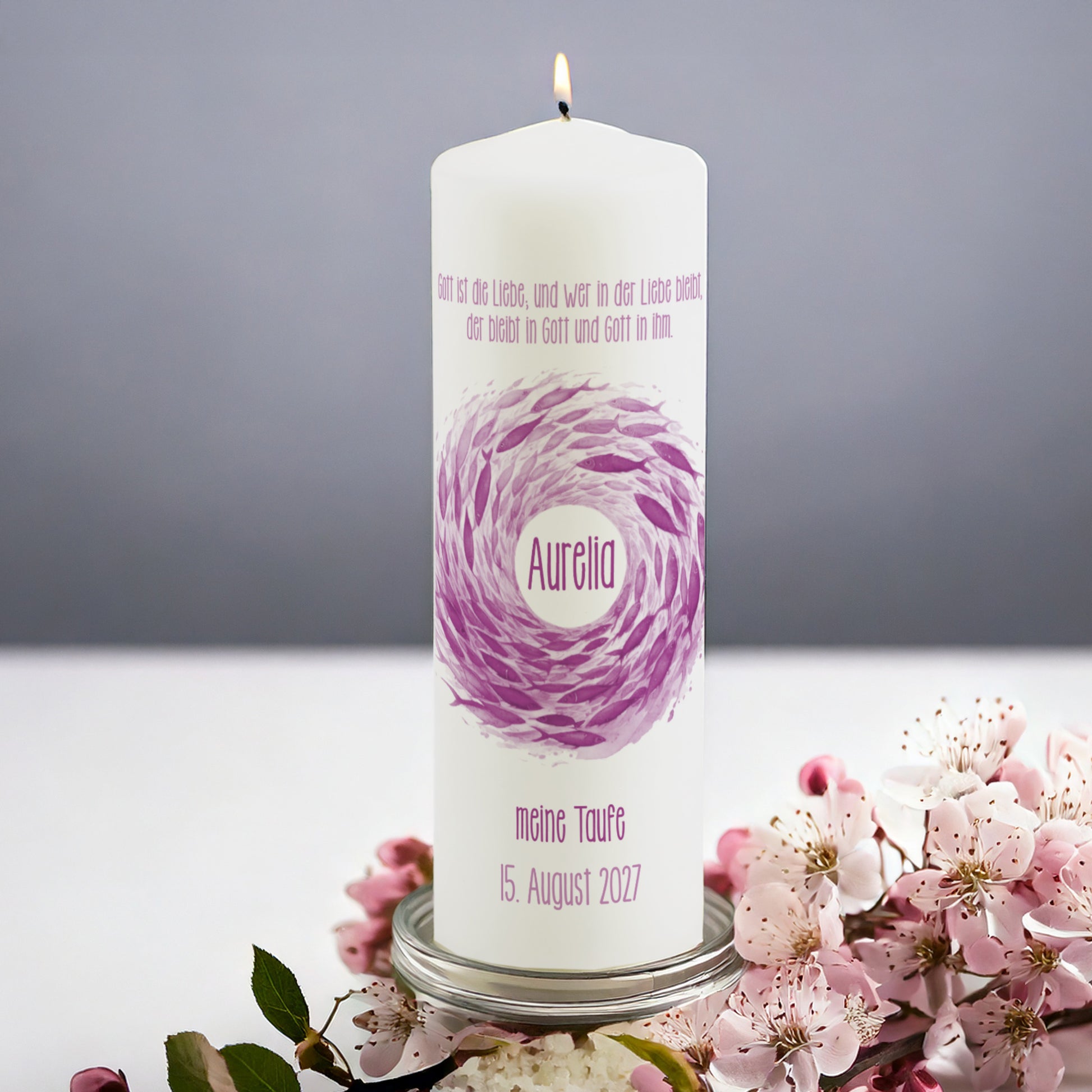 Rosa Fischschwarm-Kerze zur Taufe mit personalisiertem Namen – Eine zart gestaltete Taufkerze mit einem schwungvollen Fischschwarm in Violett- und Rosatönen. In der Mitte befindet sich der Name des Täuflings, während oben ein biblischer Spruch zur Liebe abgebildet ist. Die Beschriftung „Meine Taufe“ und das Datum sind unterhalb des Motivs. Die Kerze steht auf einem silbernen Halter, umgeben von blühenden rosa Kirschblüten.