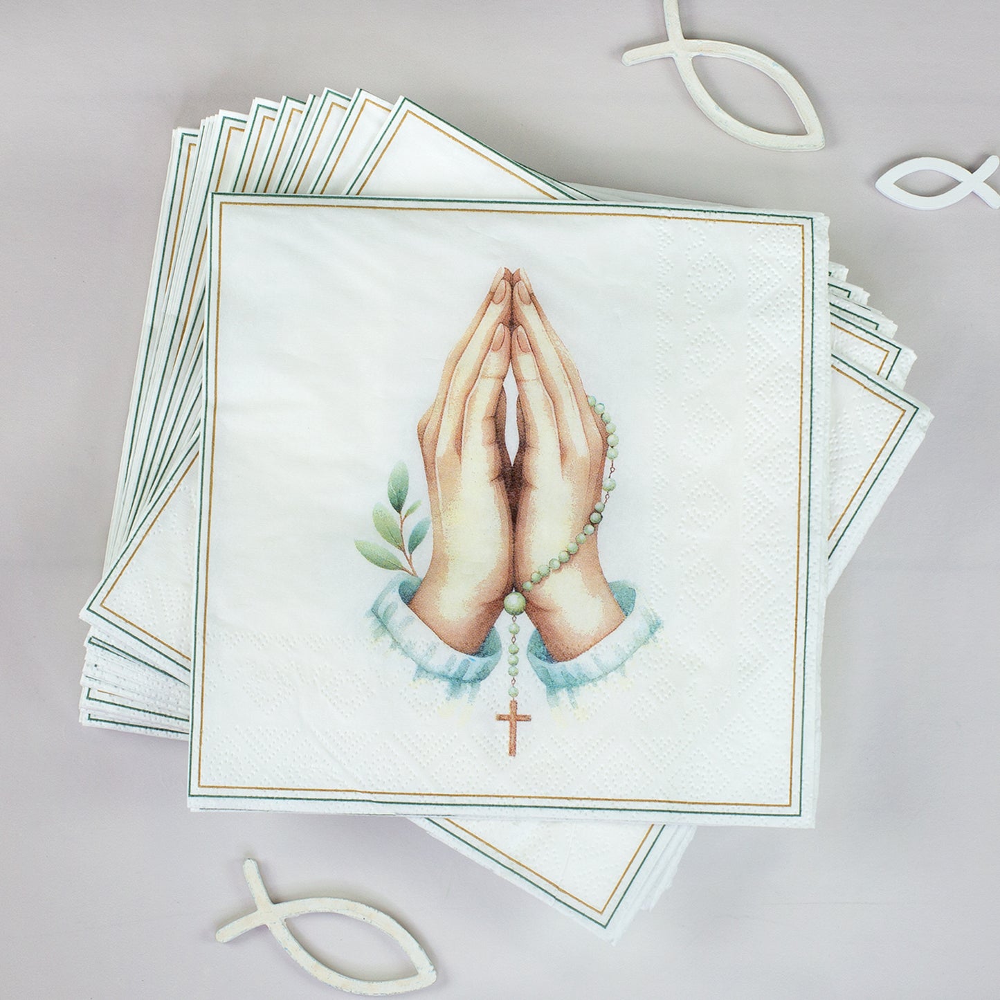 Stapel Servietten mit betenden Händen, Rosenkranz und Kreuz neben christlichen Fischsymbolen