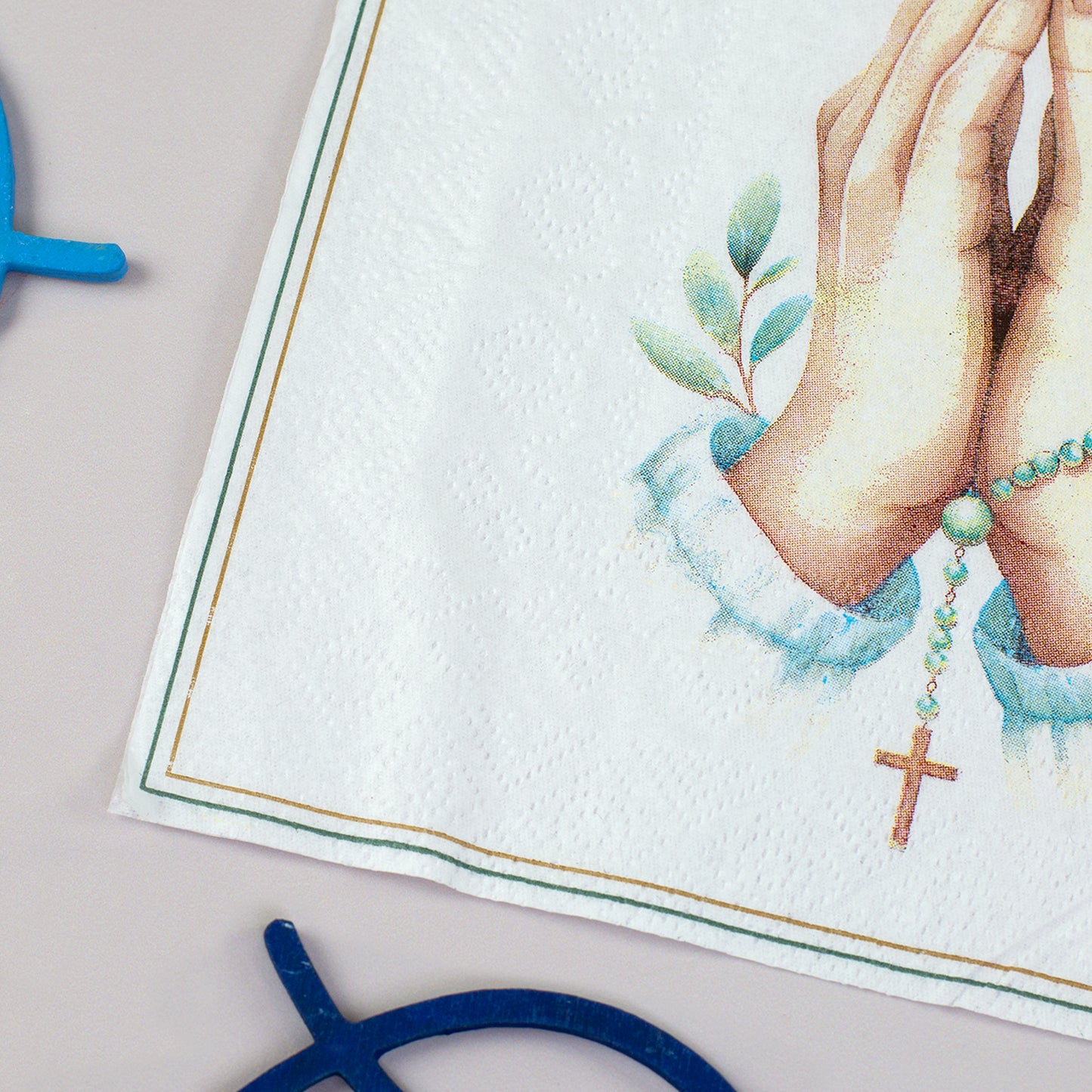 Detailaufnahme der Serviette mit feinem Rahmen und christlichem Motiv aus Händen, Rosenkranz und Kreuz