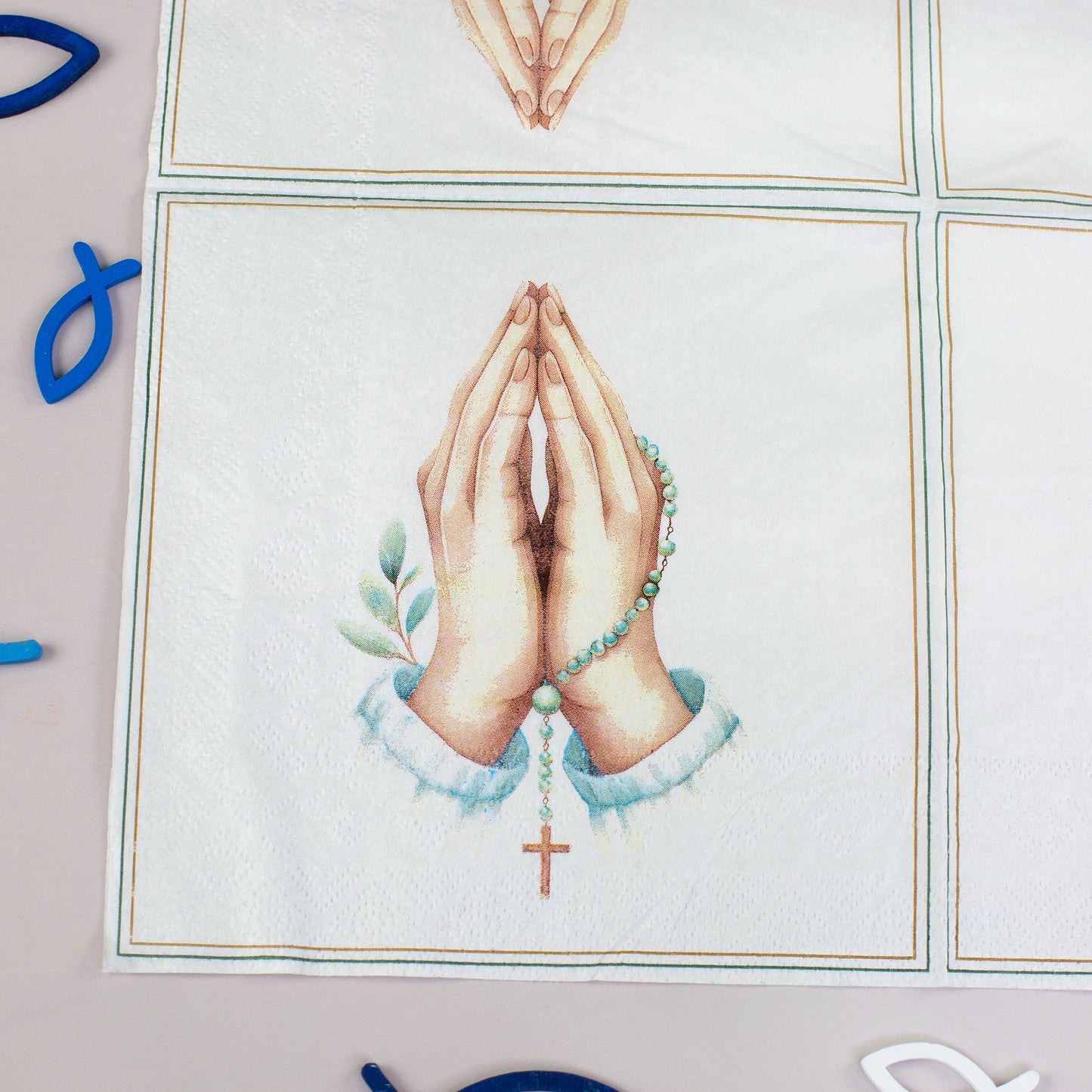 Nahaufnahme einer Serviette mit betenden Händen, Rosenkranz, Kreuz und blau-weißer christlicher Dekoration