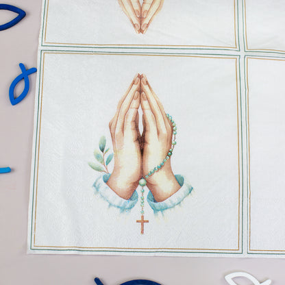 Nahaufnahme einer Serviette mit betenden Händen, Rosenkranz, Kreuz und blau-weißer christlicher Dekoration