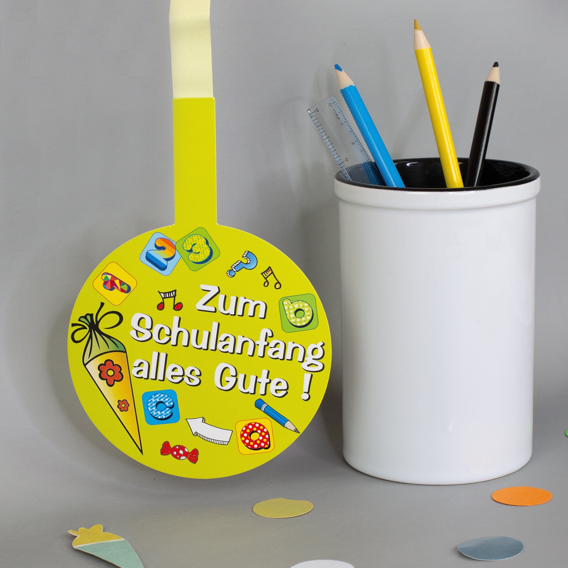 Gelber Schulanfang Anhänger mit Schultüte, Stiften, Zahlen und Schulmotiven neben Stiftebecher