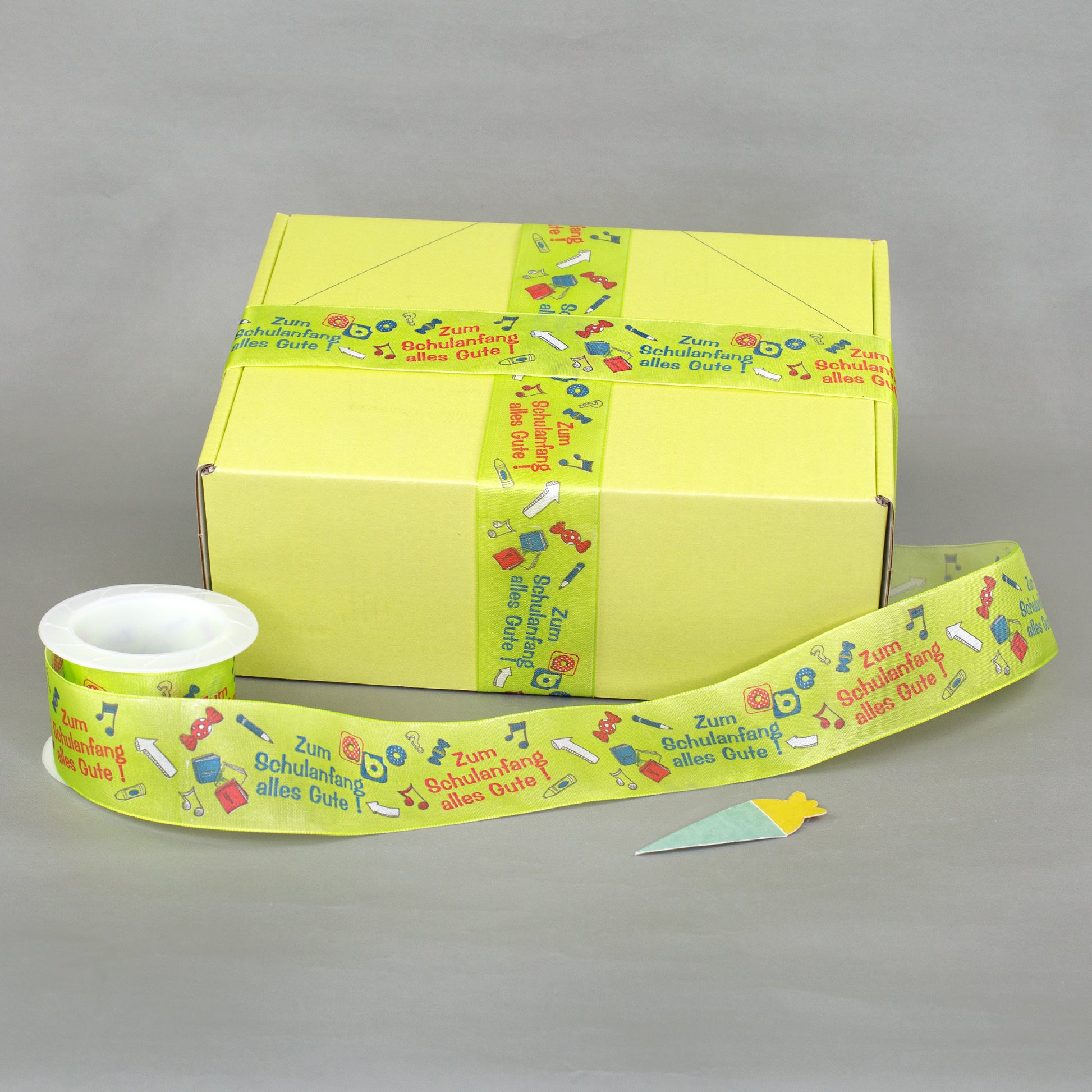 Geschenkband zur Einschulung als Dekoration an gelber Geschenkbox mit zusätzlichem Band auf Rolle