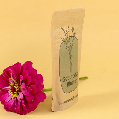 Seitliche Ansicht vom Anzuchtset Geburtstagsblumen im Kraftpapierbeutel mit pinker Blume daneben